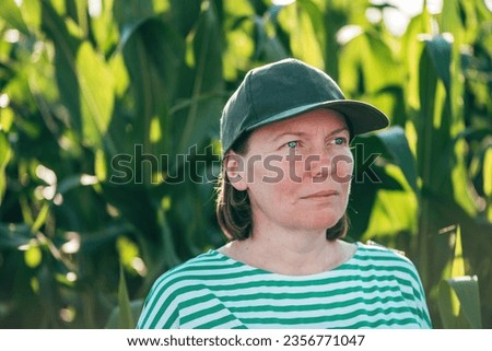Portrait of female farmer with trucker's hat standing in lush green corn crop field with serious face expression, selective focus Royalty-Free Stock Photo #2356771047