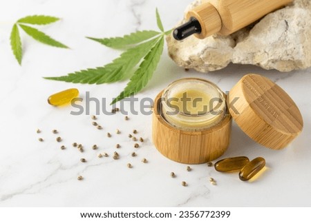 Hemp salve for joints and muscles in open glass wooden jar and relaxing CBD serum oil in dropper bottle  and in capsules as a complex in the treatment of the musculoskeletal system. Cannabis products Royalty-Free Stock Photo #2356772399