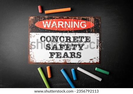 Concrete safety fears. Metal warning sign and colored pieces of chalk on a dark chalkboard background.