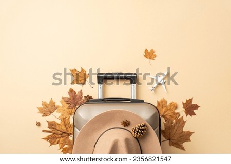 Planning an autumn getaway? Behold a top view image of a gray suitcase with autumn leaves around and a charming felt hat on a soothing beige background, perfect for your advertisement or text Royalty-Free Stock Photo #2356821547
