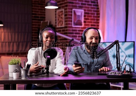 African american woman and cohost during online show in neon lights studio, shooting vlog using professional recording tools. Vloggers talking with fans during live broadcast