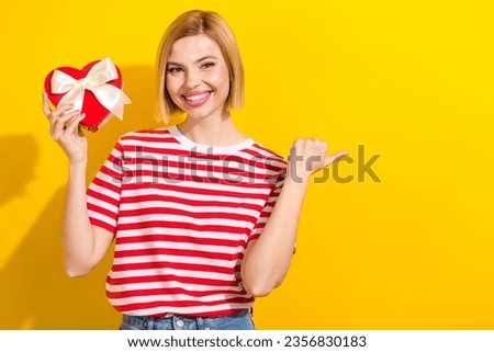 Photo of satisfied lovely woman dressed striped t-shirt hold heart box look directing empty space isolated on vibrant yellow background