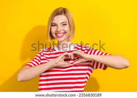 Portrait of adorable cheerful girl with bob hairdo wear stylish t-shirt showing heart symbol on chest isolated on bright yellow background