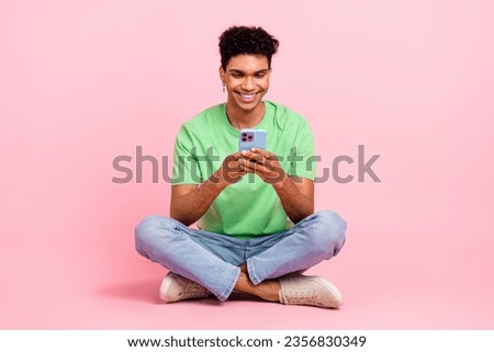 Full size photo of cheerful guy dressed green t-shirt sitting on floor look at smartphone read email isolated on pink color background