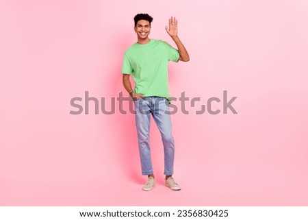Full size photo of cheerful positive guy with piercing dressed green t-shirt jeans waving palm say hi isolated on pink color background