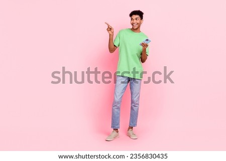Full size photo of impressed guy dressed green t-shirt look directing at empty space smartphone in hand isolated on pink color background