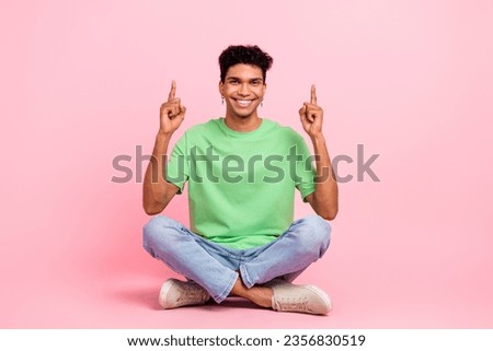 Full size photo of positive guy dressed green t-shirt sit on floor indicating at empty space proposition isolated on pink color background