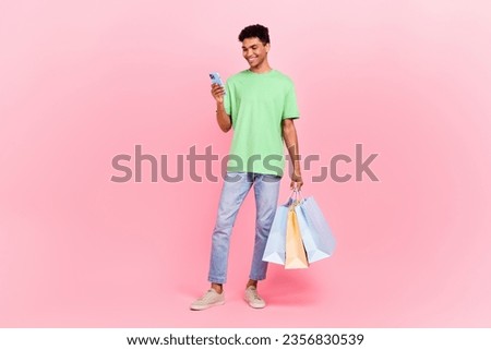 Full size photo of cheerful cool guy dressed green t-shirt hold new clothes read email on smartphone isolated on pink color background