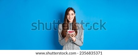 Beautiful girl holding birthday cake and celebrating, wishing happy bday and smiling, standing against blue background.