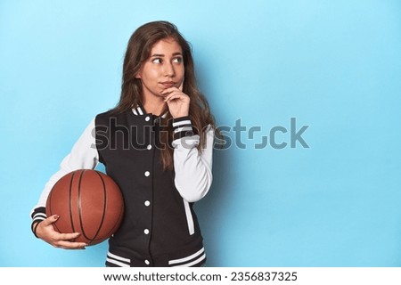 Stylish teen with basketball, embracing sports fashion looking sideways with doubtful and skeptical expression.