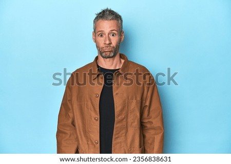 Middle-aged caucasian man on blue backdrop sad, serious face, feeling miserable and displeased.