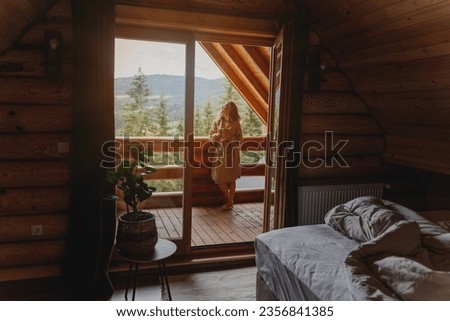 Young relaxed cheerful woman enjoying the morning and nature on the cottage balcony at sunrise with a cup of tea Royalty-Free Stock Photo #2356841385