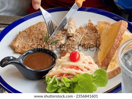 a photography of a plate of food with a fork and knife, plate of food with a fork and knife and a cup of sauce.