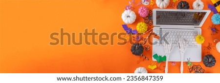 Funny Halloween bright yellow composition. White laptop with typing skeleton hands, Halloween decor colorful holiday accessories - spiders, cobwebs, pumpkins, bats, top view copy space banner Royalty-Free Stock Photo #2356847359