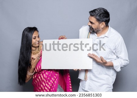 Indian couple holding white board, promoting offers on festival season while wearing traditional cloths, standing isolated over plain background