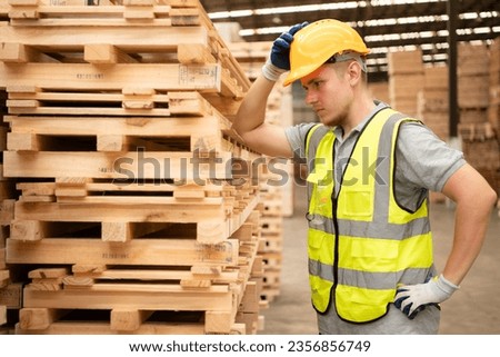 Portrait of warehouse worker checking stock of wooden pallets in storage warehouse.
