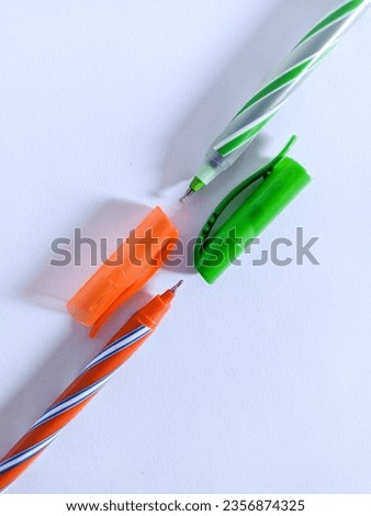 Two green and orange pens are photographed on a plain white background