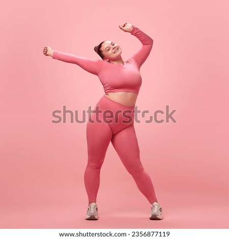 Full length happy young attractive plus size active woman in pink top and leggins warm up, training armes isolated studio background. Concept of workout, sport, motivation and body positivity