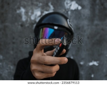 Photo of an index finger pressing a button on a remote with a blurred background of an unknown man in an all-black costume, "SHOTLISTstream".