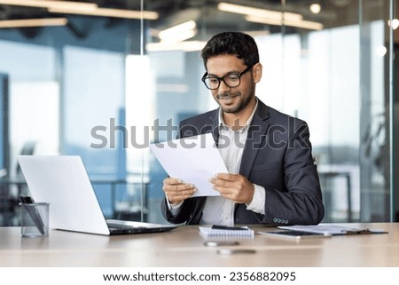 Experienced young financier at workplace checking and reading company financial report, businessman behind paper work inside office, satisfied with achievement results.