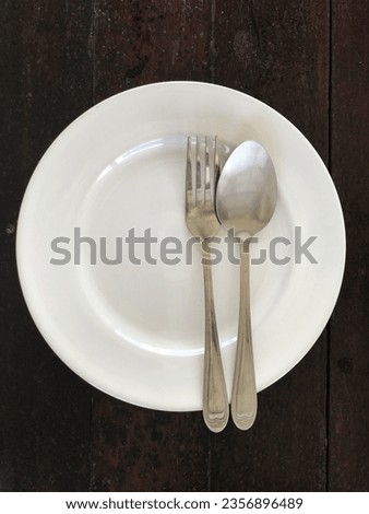 Empty white plate with spoon and fork on wooden table, stock photo