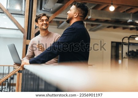 Male tech professionals having a discussion in an office. Two business men talking about a project while standing on an interior balcony. Royalty-Free Stock Photo #2356901197