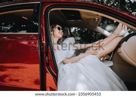 Beautiful smiling young blonde bride with a bouquet in sunglasses sits in a red car. Wedding photography, portrait, lifestyle.