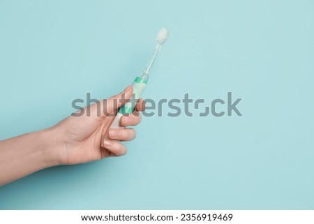 Woman holding electric toothbrush on light blue background, closeup. Space for text
