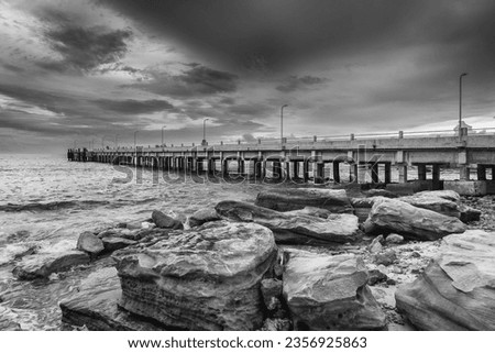 Tranquil Beauty: Black and white picture of Pier Bridge Extending into the Sea, Embracing Thailand's Eastern Island's Rocky Shores as day time.