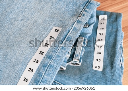Close up shot of a couple's matching blue jeans of different sizes on wooden background.  Royalty-Free Stock Photo #2356926061