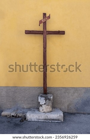 text reads "INRI" stunning old wooden cross in village traditional religious icon iconography crucifixion passion symbol powerful rustic faded isolated yellow wall Jesus no one believes anymore 