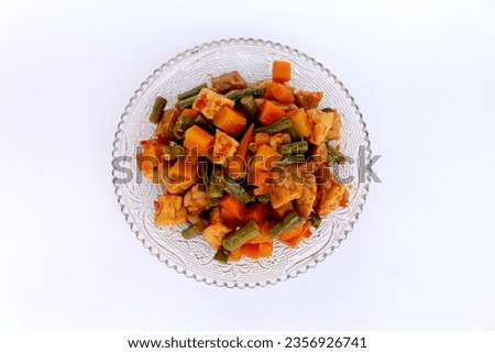 Stir-fried tempeh, green beans, carrots are a typical Indonesian food or side dish which is generally eaten with rice. With a white background and negative space.