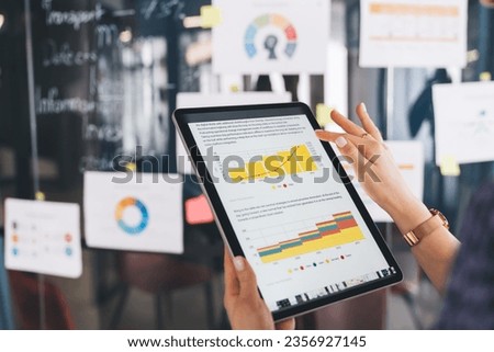 Unrecognizable female marketer checking financial report with infographics while browsing web document on modern touch pad, cropped entrepreneur with digital tablet reading business information Royalty-Free Stock Photo #2356927145