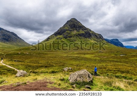 A hiker on a trail in front of a mountain under a grey, stormy sky Royalty-Free Stock Photo #2356928133