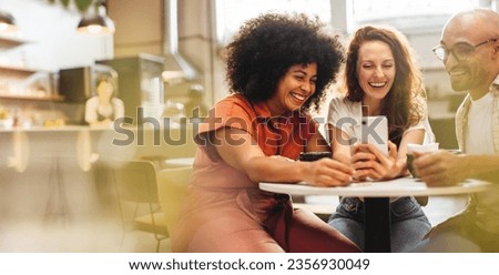 Group of friends having fun and making a video call, enjoying coffee and wi-fi at a local café. Happy young people hanging out together over a social lunch on the weekend. Royalty-Free Stock Photo #2356930049
