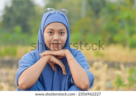 Indonesian woman in hijab in blue dress with relaxed facial expressions and smiling against a natural background