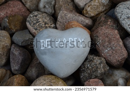 a gray heart with the inscription be happy lies on colored stones