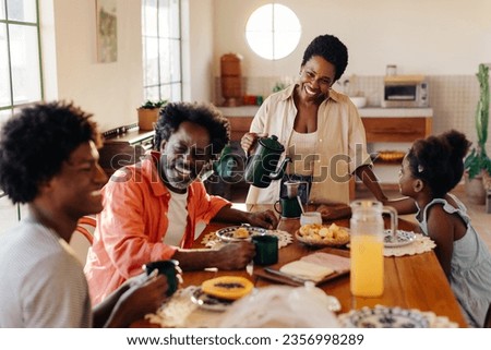 Afro Brazilian family happily gathers for a breakfast filled with pão de queijo and drip coffee. Mother serving her family a traditional breakfast with smiles, love, and togetherness at home. Royalty-Free Stock Photo #2356998289