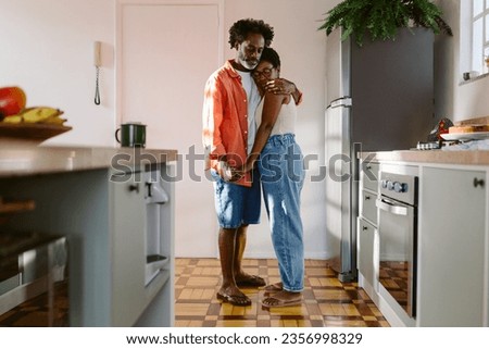Affectionate Brazilian couple at home, standing in the kitchen, embracing and holding hands. A genuine moment of love and connection between a mature husband and wife. Royalty-Free Stock Photo #2356998329
