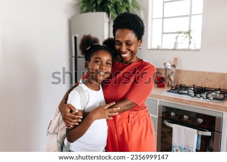 Black mother holding her daughter in her warm arms as she says goodbye on a school morning. Happy parent showing her child love and affection, preparing her for the day ahead. Royalty-Free Stock Photo #2356999147