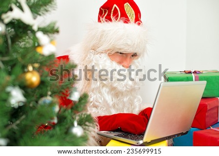 Santa Claus is using laptop at his workshop.