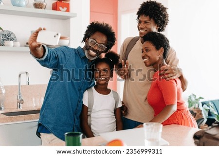 Father taking a selfie of his family with his smartphone, capturing their happy moment before leaving the house for work and school. Black family standing in their kitchen during their morning routine
