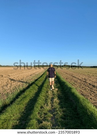 Lost in the vastness of rural beauty, a solitary figure walks through endless fields of green. Amidst the whispers of the wind and the rustling of crops, a tranquil moment of connection with nature un Royalty-Free Stock Photo #2357001893