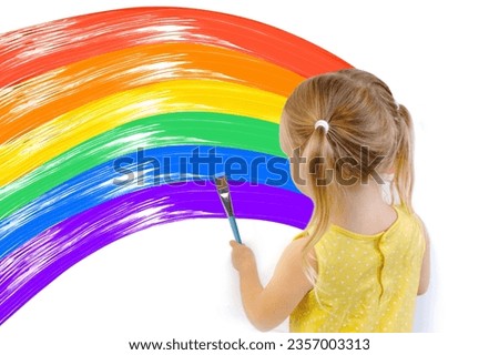 small child, blonde girl 3 years in yellow dress paints with brush multi-colored rainbow, flowers on white wall, childish naive drawing, gouache, acrylic, happiness childhood, creative development Royalty-Free Stock Photo #2357003313