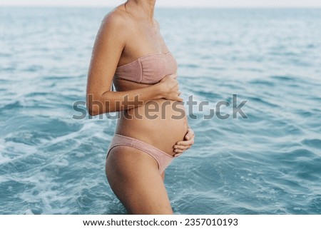 Portrait of an unrecognizable pregnant woman in a swimsuit on the seashore.