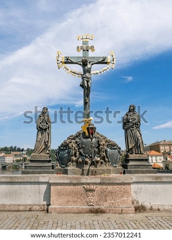 Metal crucifix scene installed in 17th century on Charles Bridge is flanked by 19th century sandstone statues of Mary and John the Evangelist. The Hebrew gold letters are from medieval anti-semitism. Royalty-Free Stock Photo #2357012241