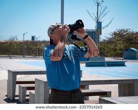 A White Man Wearing a Cap Takes a Picture with his Camera of a Bird Flying in the Sky