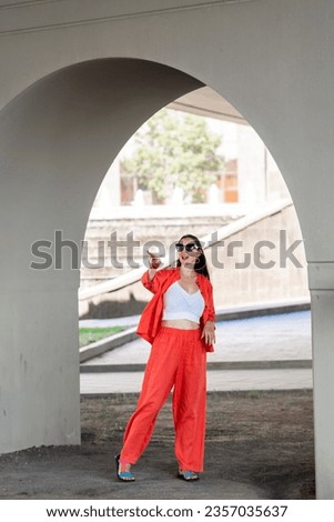 Summer portrait of a girl with long blond hair. A girl in orange clothes and sunglasses stands on the street. High quality photo