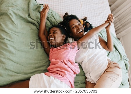 A joyful black family, a mother and daughter, bonding together and having fun at home. They laugh, hold hands, and share quality time, creating a warm and playful atmosphere. Royalty-Free Stock Photo #2357035901