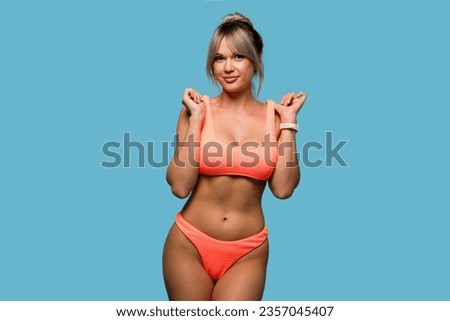 Slim woman posing wearing orange swimsuit on blue background. Sporty girl in good shape has thin body, smooth healthy skin, slender legs. Perfect female figure without cellulite